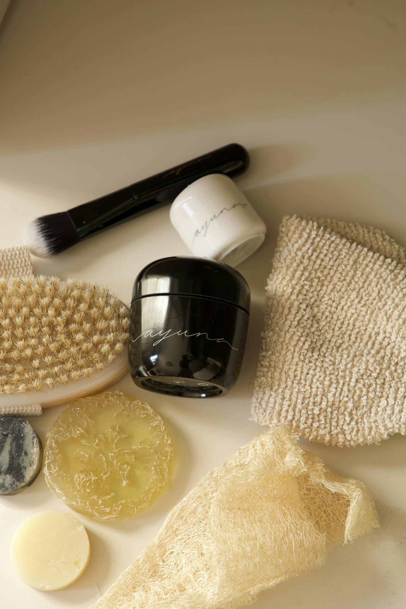 A flat lay of natural skincare products including jars, brushes, and sponges on a neutral background.